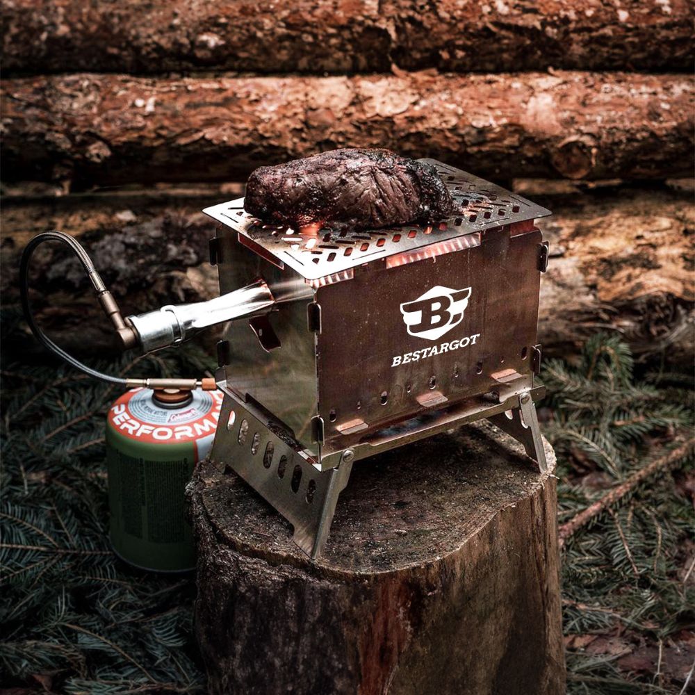 Ein tragbarer Campingkocher von BESTARGOT, der auf einem Baumstumpf steht und ein Steak im Freien brät, mit angeschlossenem Propangasbehälter. Die Szene spielt in einem bewaldeten Gebiet mit Baumstämmen im Hintergrund.