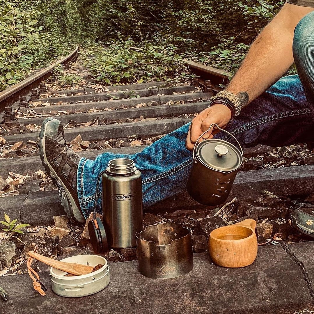 A man sits by the railroad tracks and pours coffee